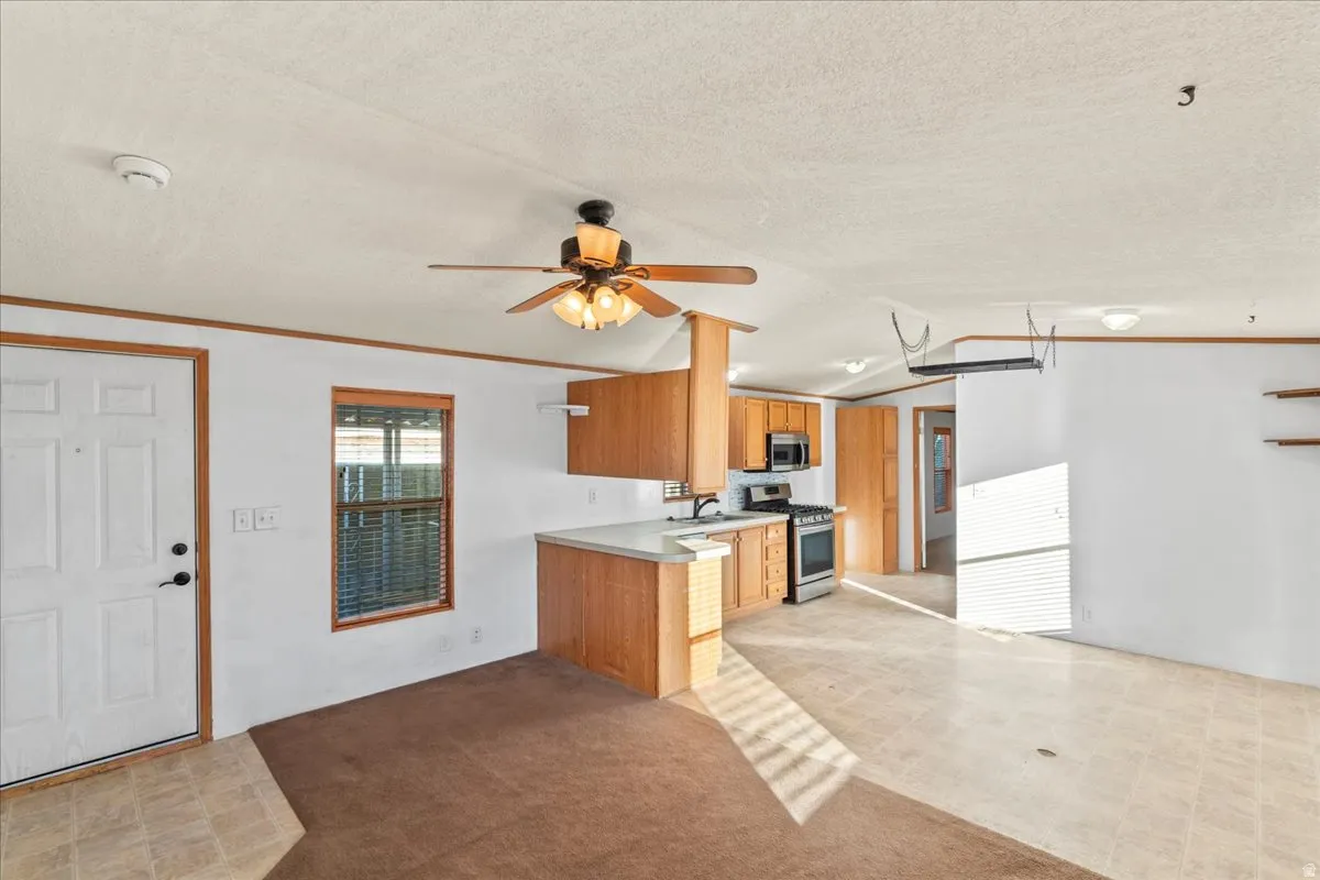 Kitchen with light countertops, stainless steel appliances, open floor plan, ornamental molding, and light colored carpet
