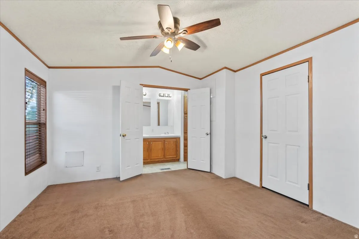 Unfurnished bedroom with lofted ceiling, ornamental molding, light colored carpet, ceiling fan, and a textured ceiling