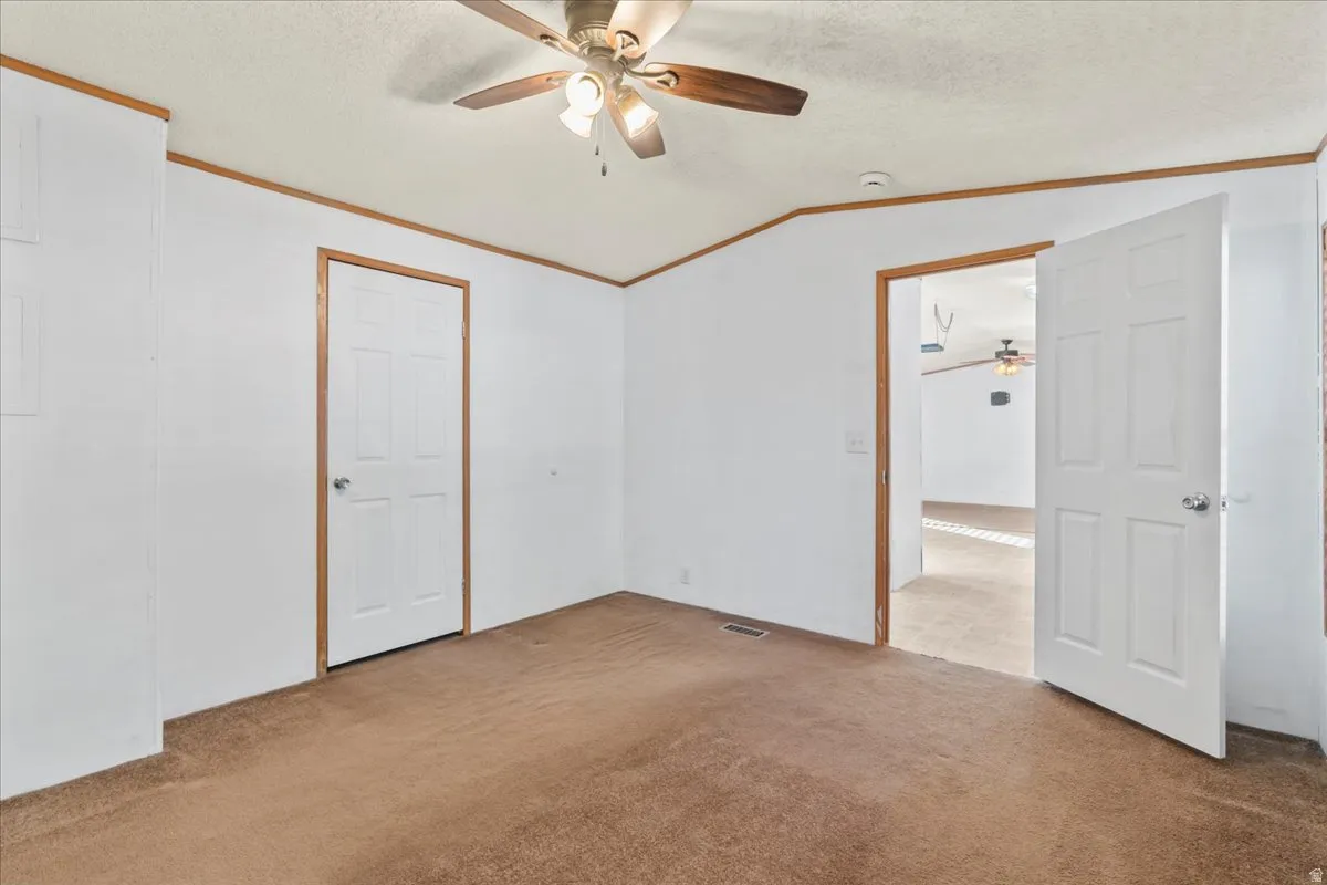 Carpeted spare room featuring a ceiling fan, crown molding, a textured ceiling, and vaulted ceiling