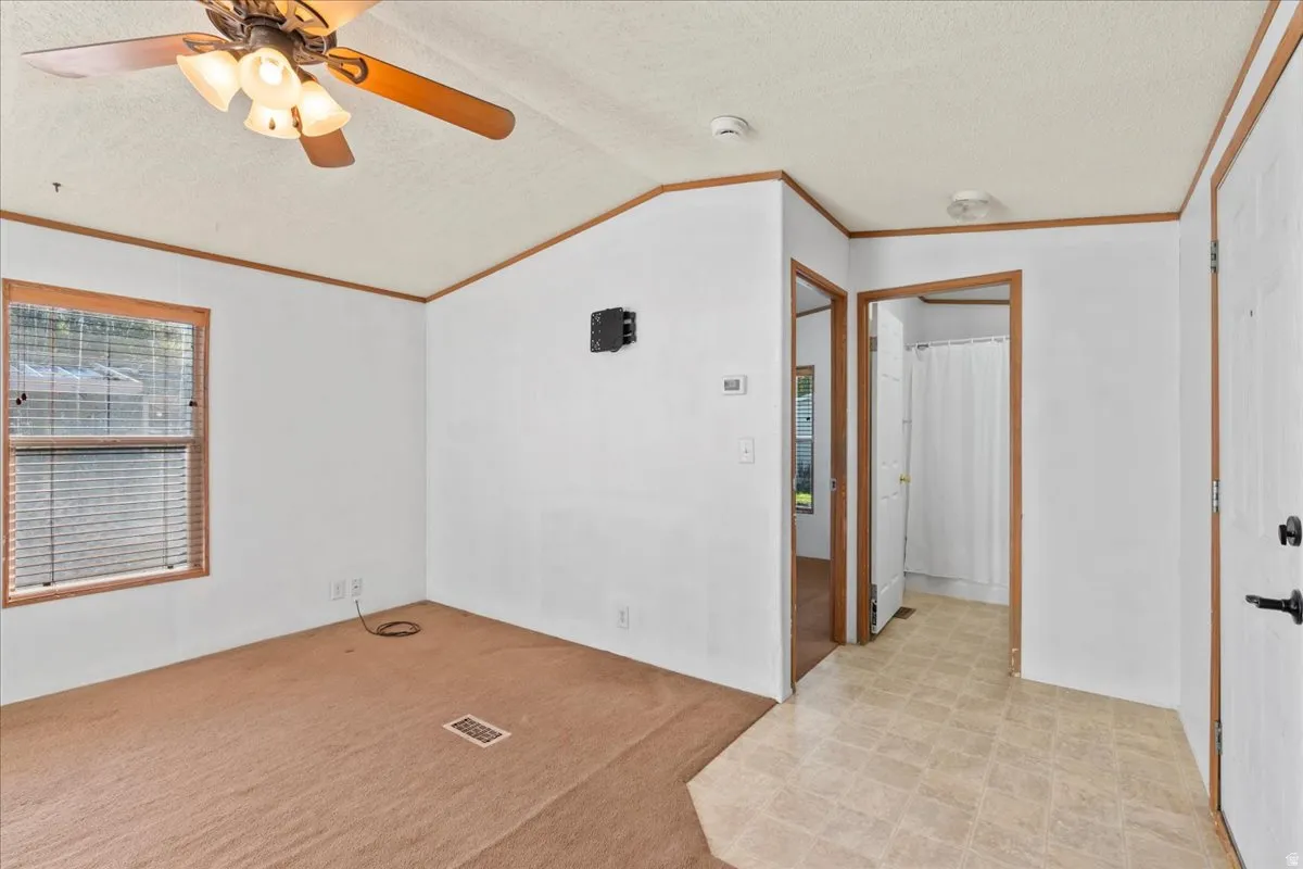 Spare room featuring ornamental molding, a textured ceiling, vaulted ceiling, light carpet, and ceiling fan