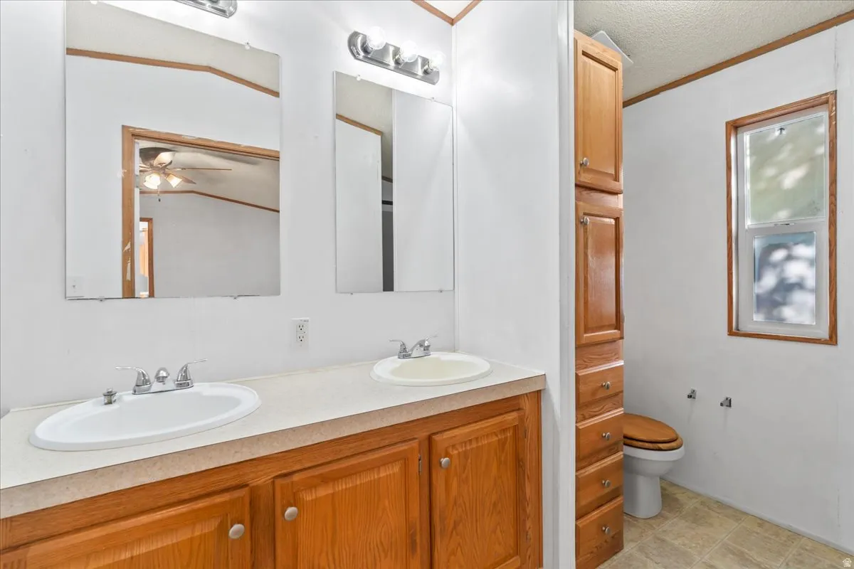 Full bath featuring double vanity, a textured ceiling, a ceiling fan, and ornamental molding