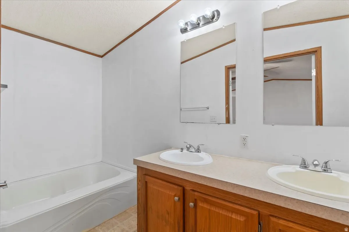 Full bath featuring ornamental molding, a bath, double vanity, a textured ceiling, and light tile patterned flooring