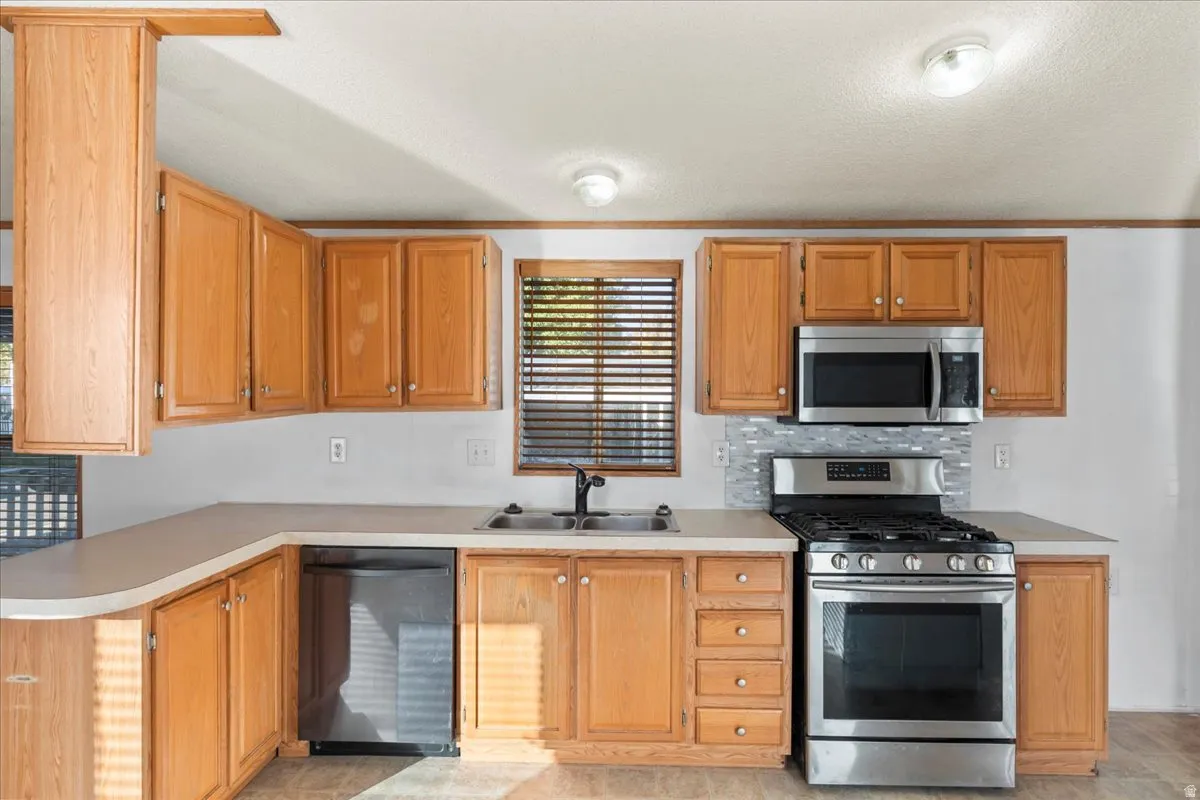 Kitchen featuring stainless steel appliances, backsplash, light countertops, a textured ceiling, and brown cabinetry