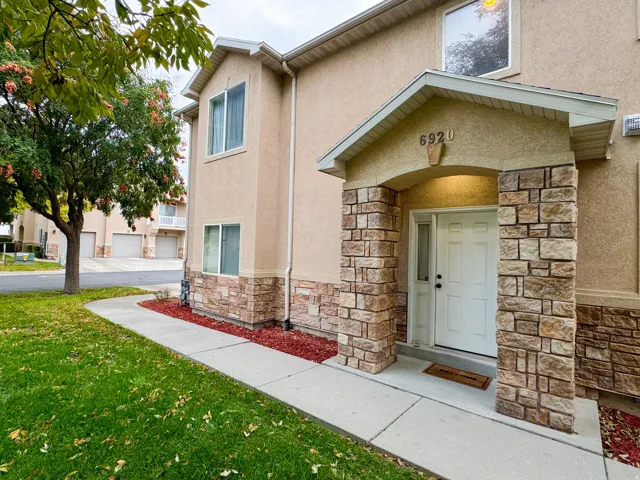 View of exterior entry with stone siding, stucco siding, and a yard