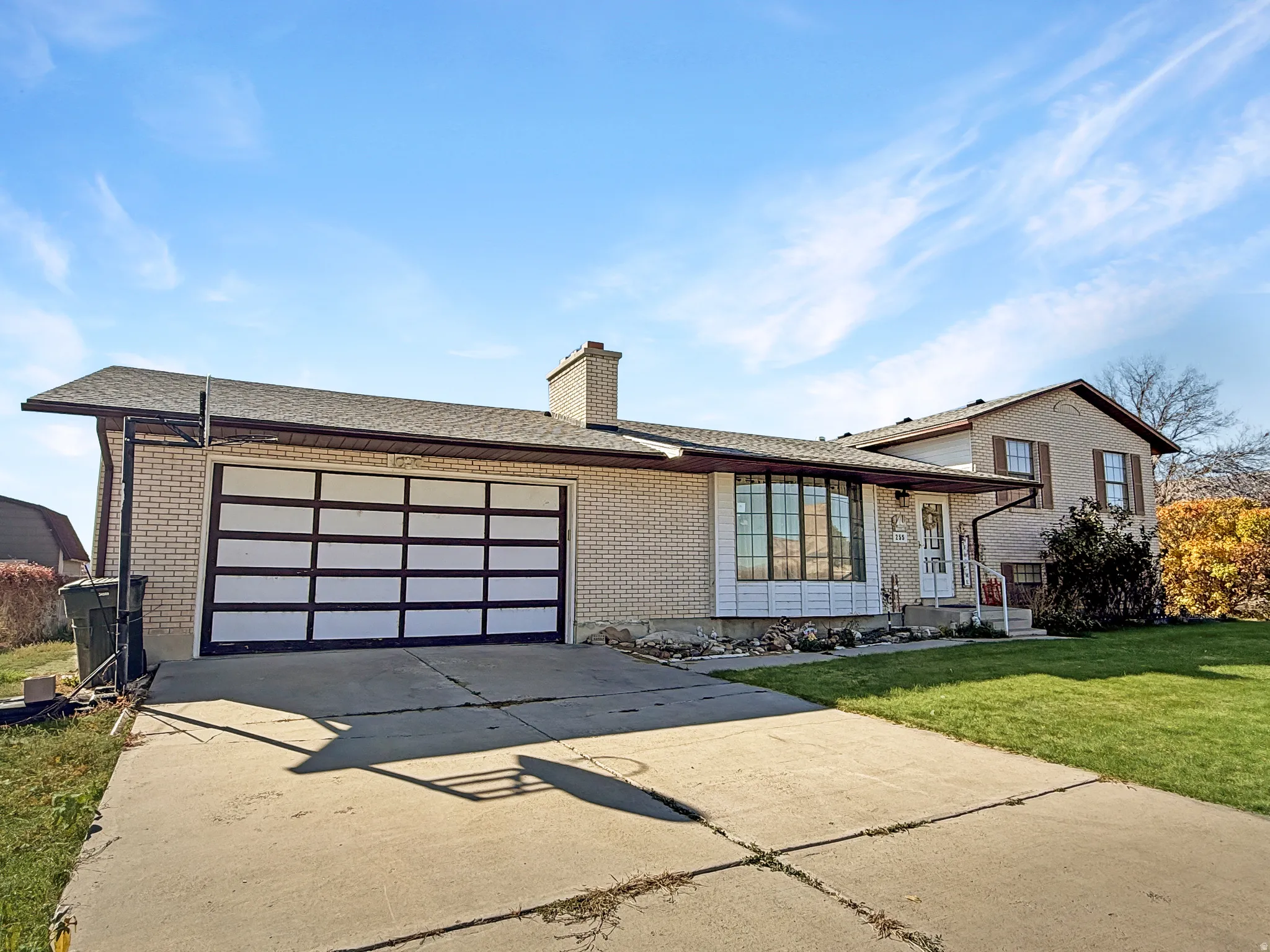 View of front of property featuring brick siding, concrete driveway, a chimney, and a front yard