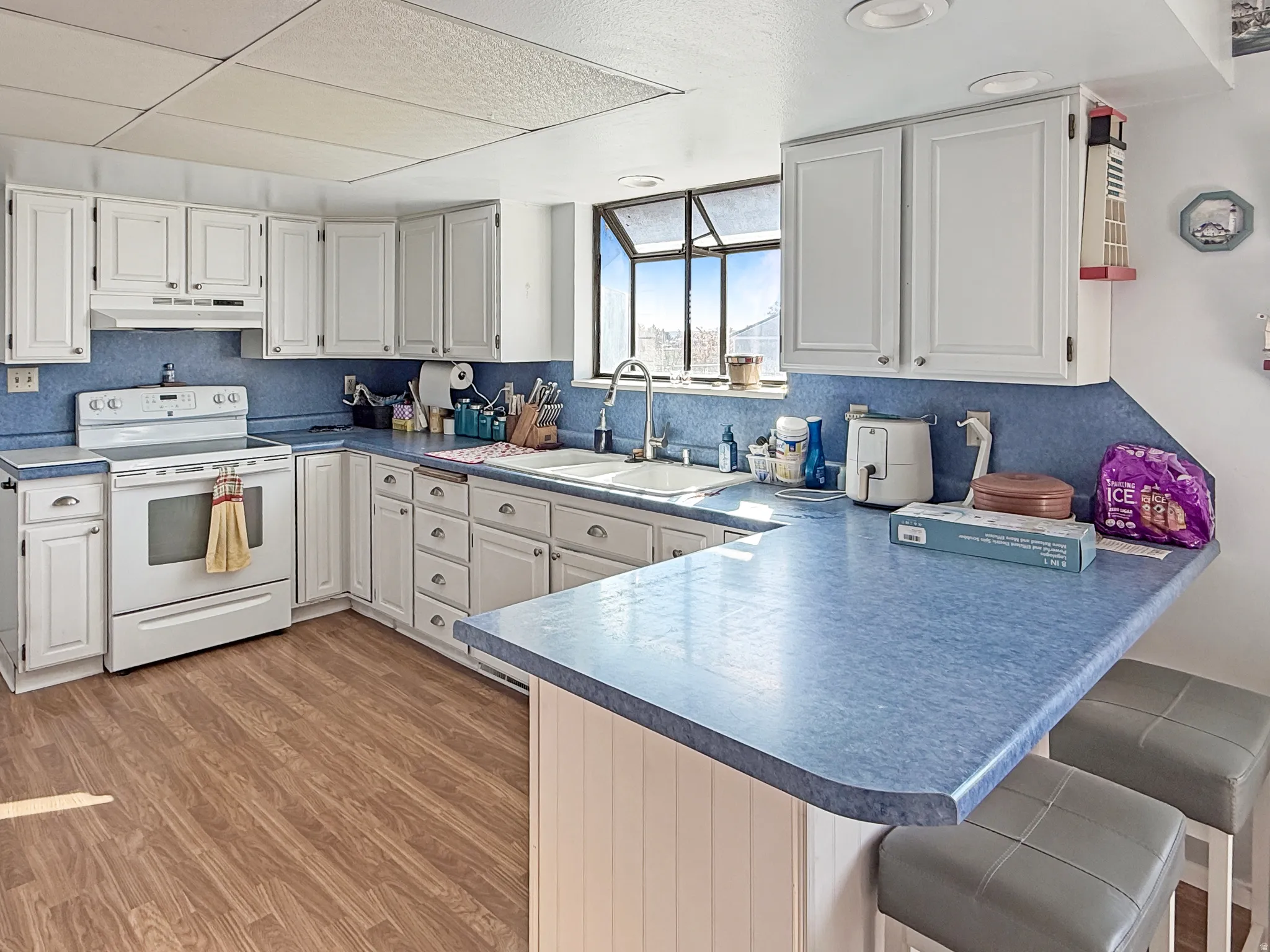 Kitchen with a kitchen bar, a peninsula, white range with electric cooktop, white cabinetry, and light wood-style floors