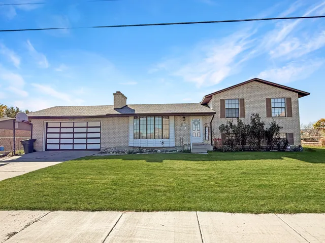 Tri-level home with brick siding, a front yard, a chimney, and driveway