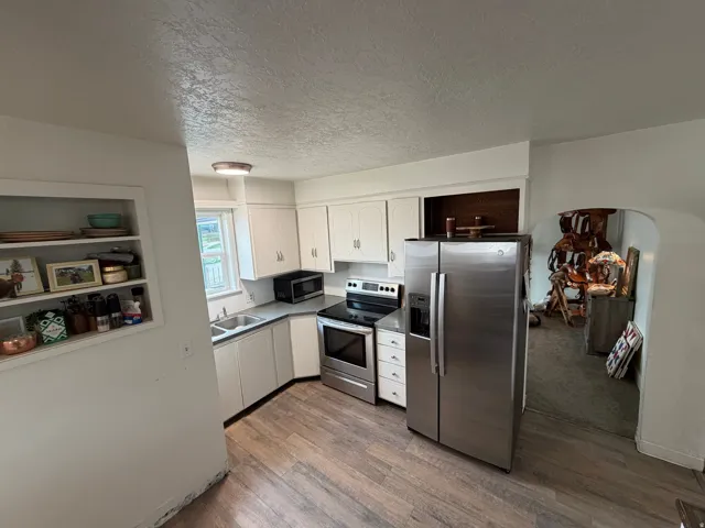 Kitchen featuring stainless steel appliances, white cabinets, arched walkways, dark wood-style floors and new flooring.