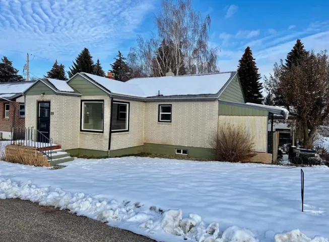 View of snowy exterior with a chimney and brick siding