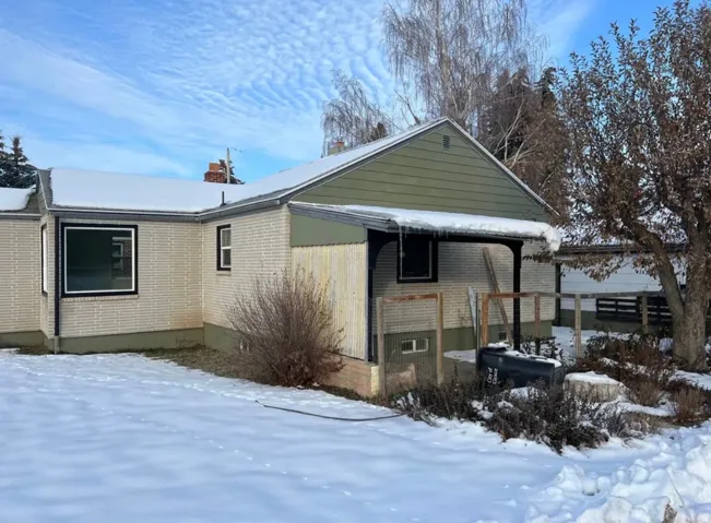 View of snowy exterior featuring brick siding and a chimney