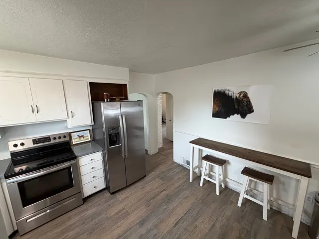 Kitchen featuring stainless steel appliances, white cabinets, arched walkways, dark wood-style floors and new flooring.