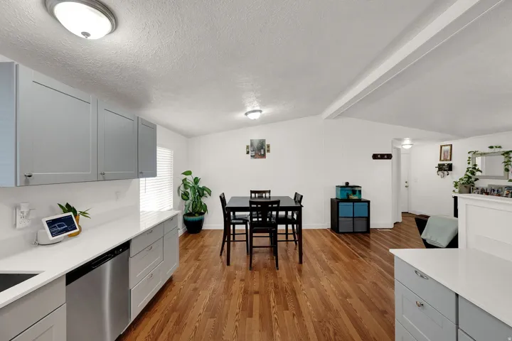 Kitchen with gray cabinetry, stainless steel dishwasher, dark wood-style floors, light stone countertops, and a textured ceiling