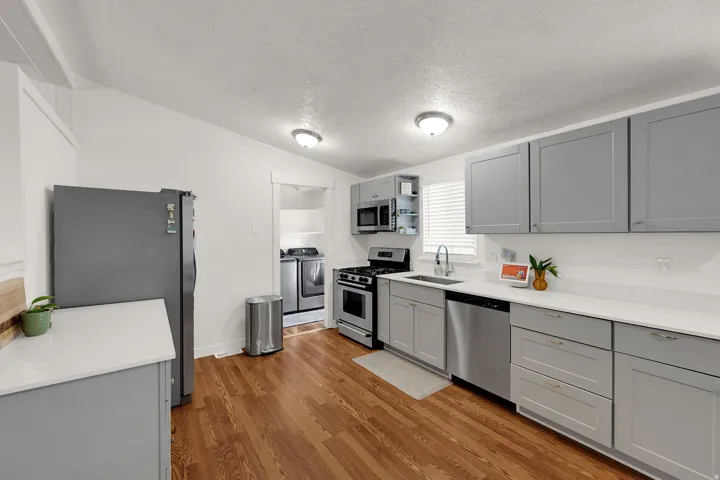 Kitchen with gray cabinets, stainless steel appliances, a textured ceiling, light wood-style floors, and washing machine and clothes dryer