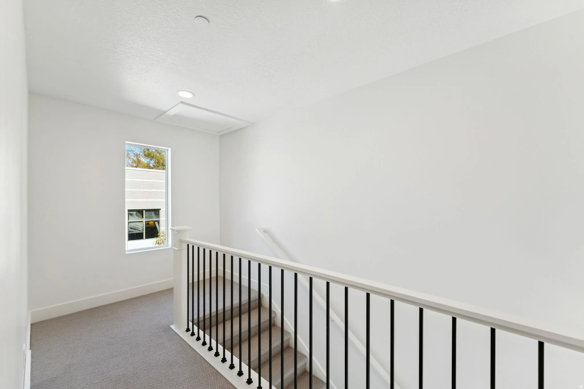 Corridor featuring light colored carpet, an upstairs landing, and a textured ceiling