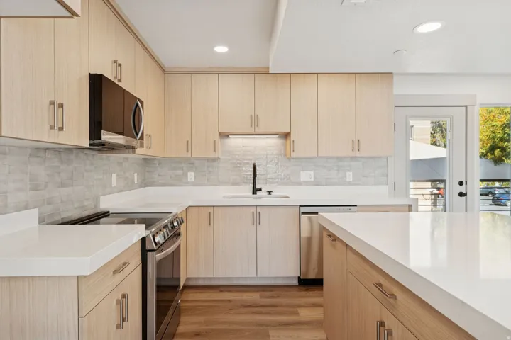 Kitchen with light brown cabinetry, stainless steel appliances, light wood-type flooring, recessed lighting, and tasteful backsplash