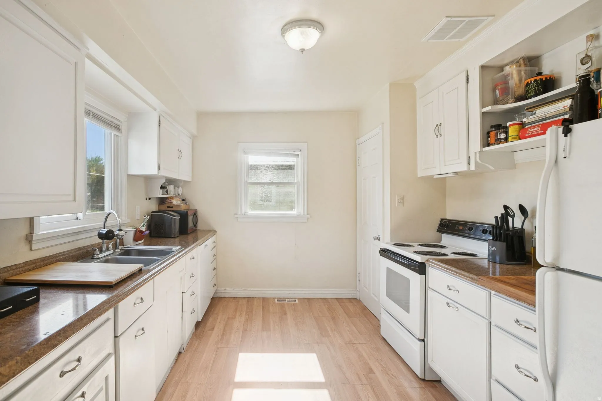Kitchen featuring white appliances, white cabinets, light wood finished floors, and dark countertops