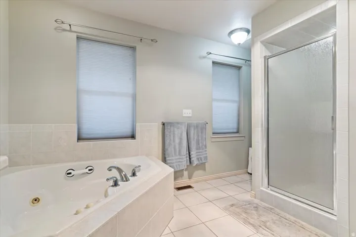 Full bath featuring light tile patterned floors, a tub with jets, and a shower stall