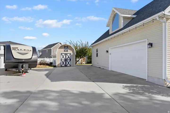 View of property exterior featuring roof with shingles, a garage, concrete driveway, and a storage unit