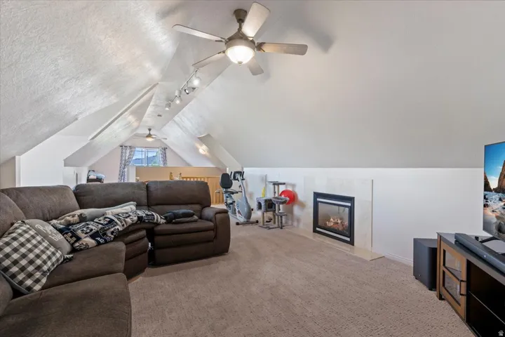 Carpeted living room with lofted ceiling, ceiling fan, rail lighting, a textured ceiling, and a high end fireplace