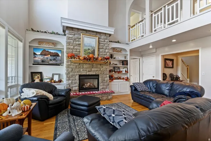 Living area with light wood-style floors, a stone fireplace, a high ceiling, and stairs
