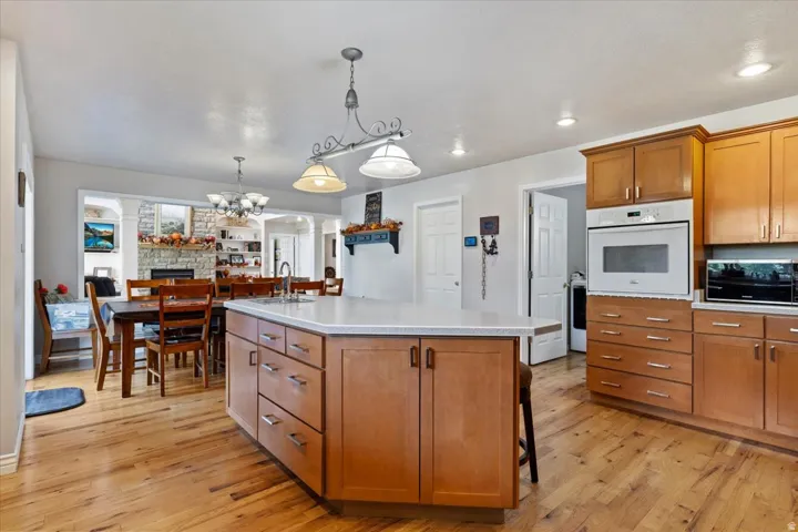 Kitchen with brown cabinetry, decorative light fixtures, white oven, a breakfast bar area, and an island with sink