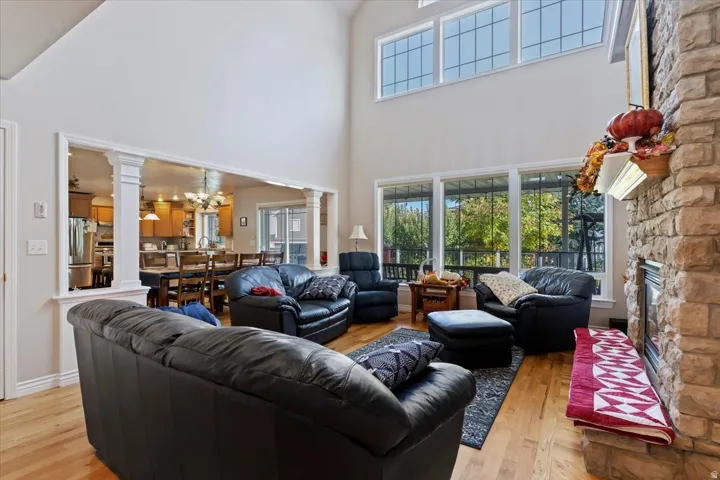 Living area featuring light wood-style flooring, decorative columns, a towering ceiling, a fireplace, and a chandelier