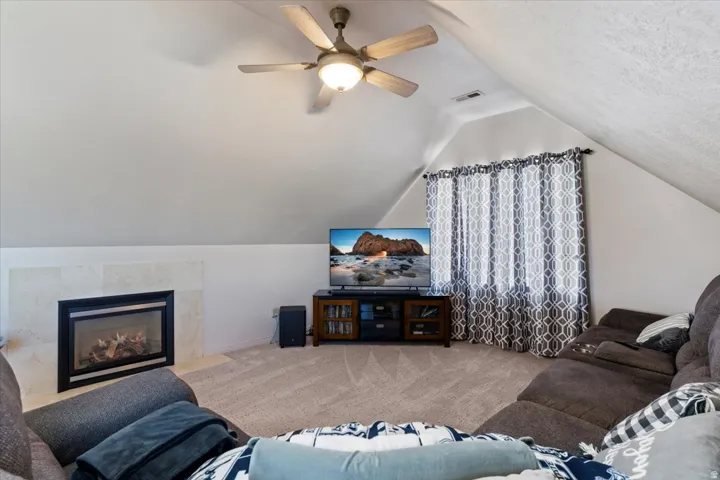 Carpeted living area featuring lofted ceiling, a fireplace, and a ceiling fan