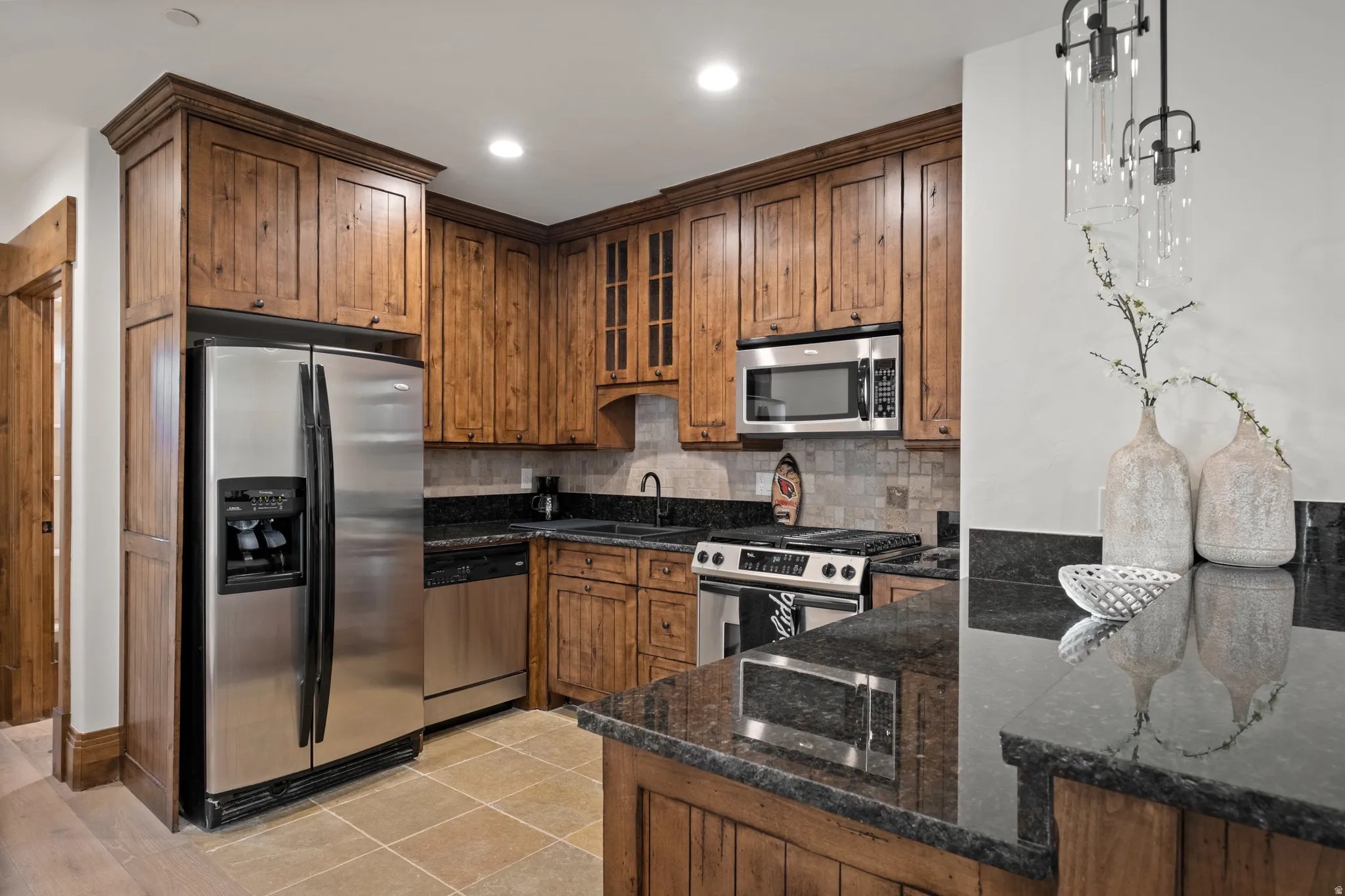 Kitchen featuring stainless steel appliances, dark stone countertops, light tile patterned floors, backsplash, and glass insert cabinets