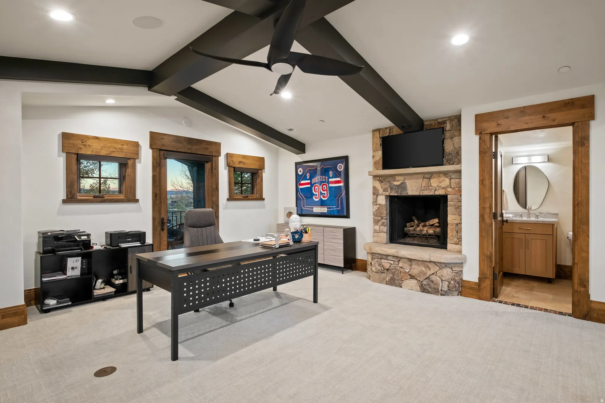 Office space with a stone fireplace, a ceiling fan, light carpet, recessed lighting, and vaulted ceiling with beams