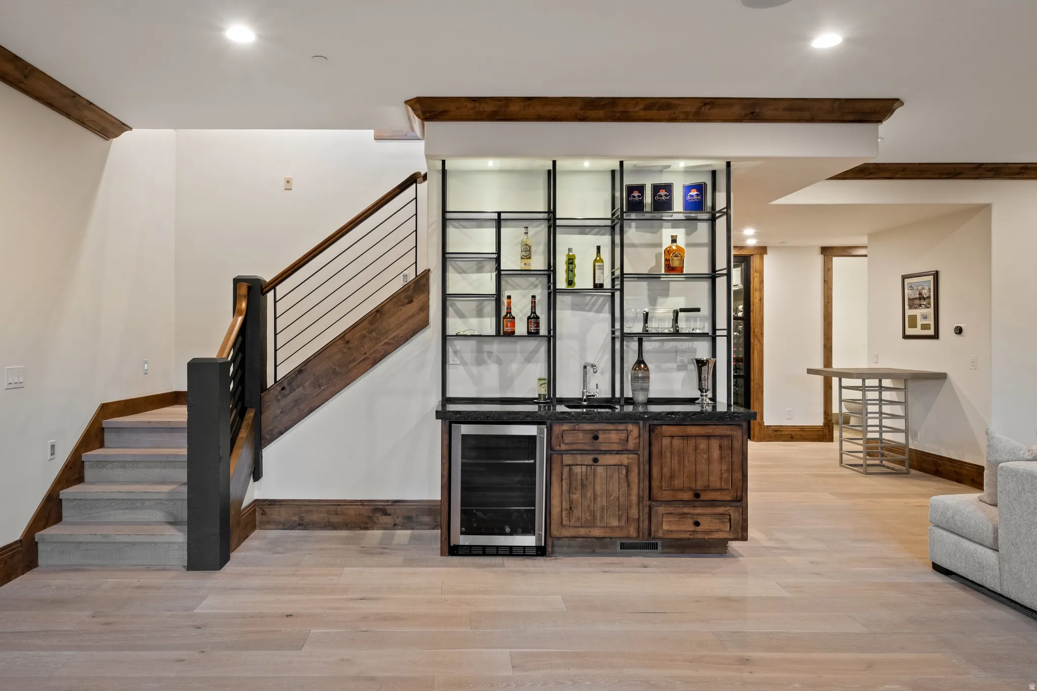 Indoor wet bar with open shelves, beverage cooler, light wood finished floors, dark stone countertops, and dark wood finish cabinets