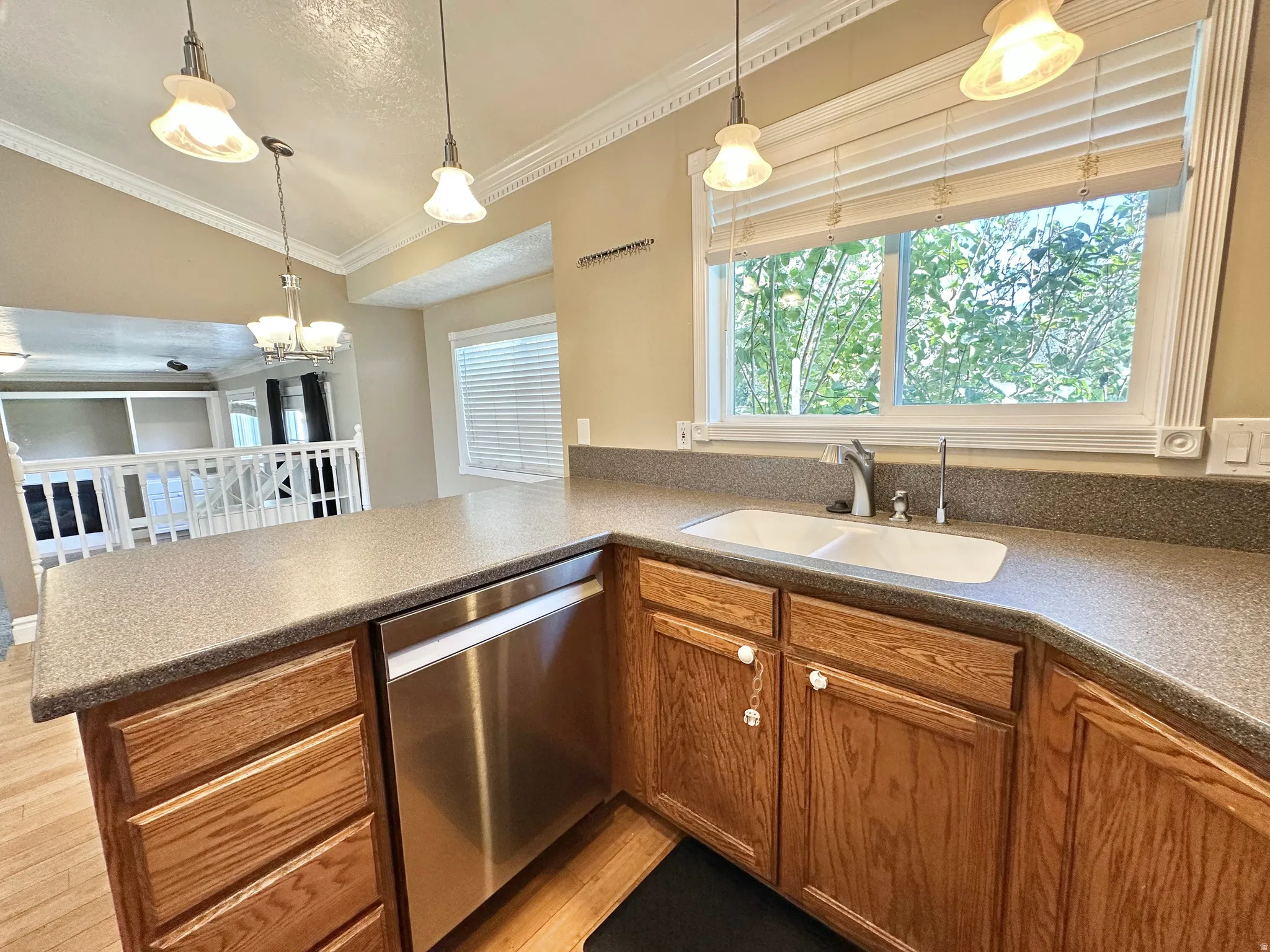 Kitchen featuring dishwasher, lighting, Corian counters, and view of greenery through window