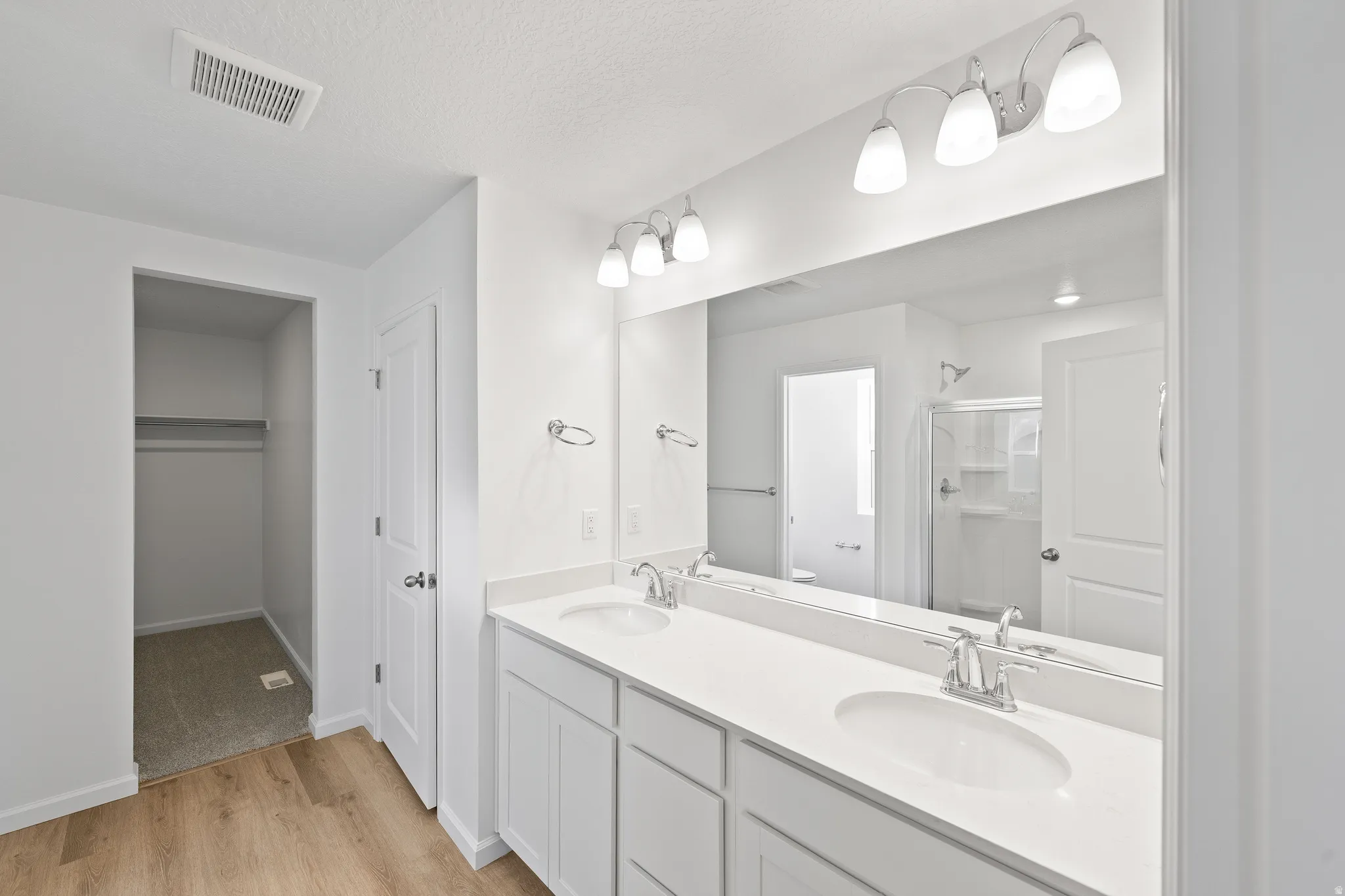 Full bathroom featuring double vanity, light wood finished floors, a stall shower, and a spacious closet