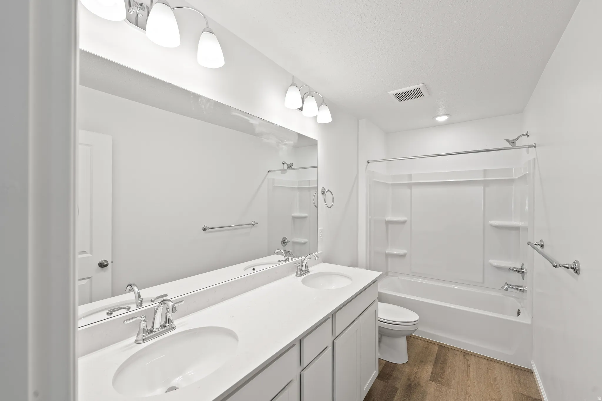 Bathroom with double vanity, dark wood-style flooring, bathing tub / shower combination, and a textured ceiling
