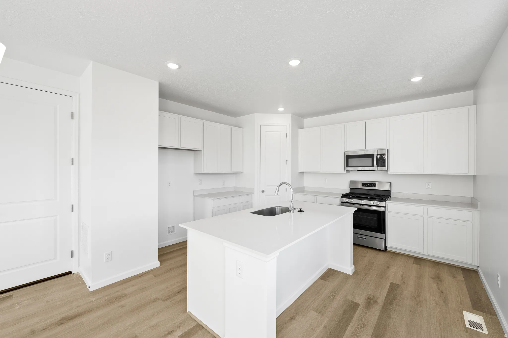 Kitchen featuring appliances with stainless steel finishes, light wood-type flooring, a center island with sink, white cabinets, and recessed lighting