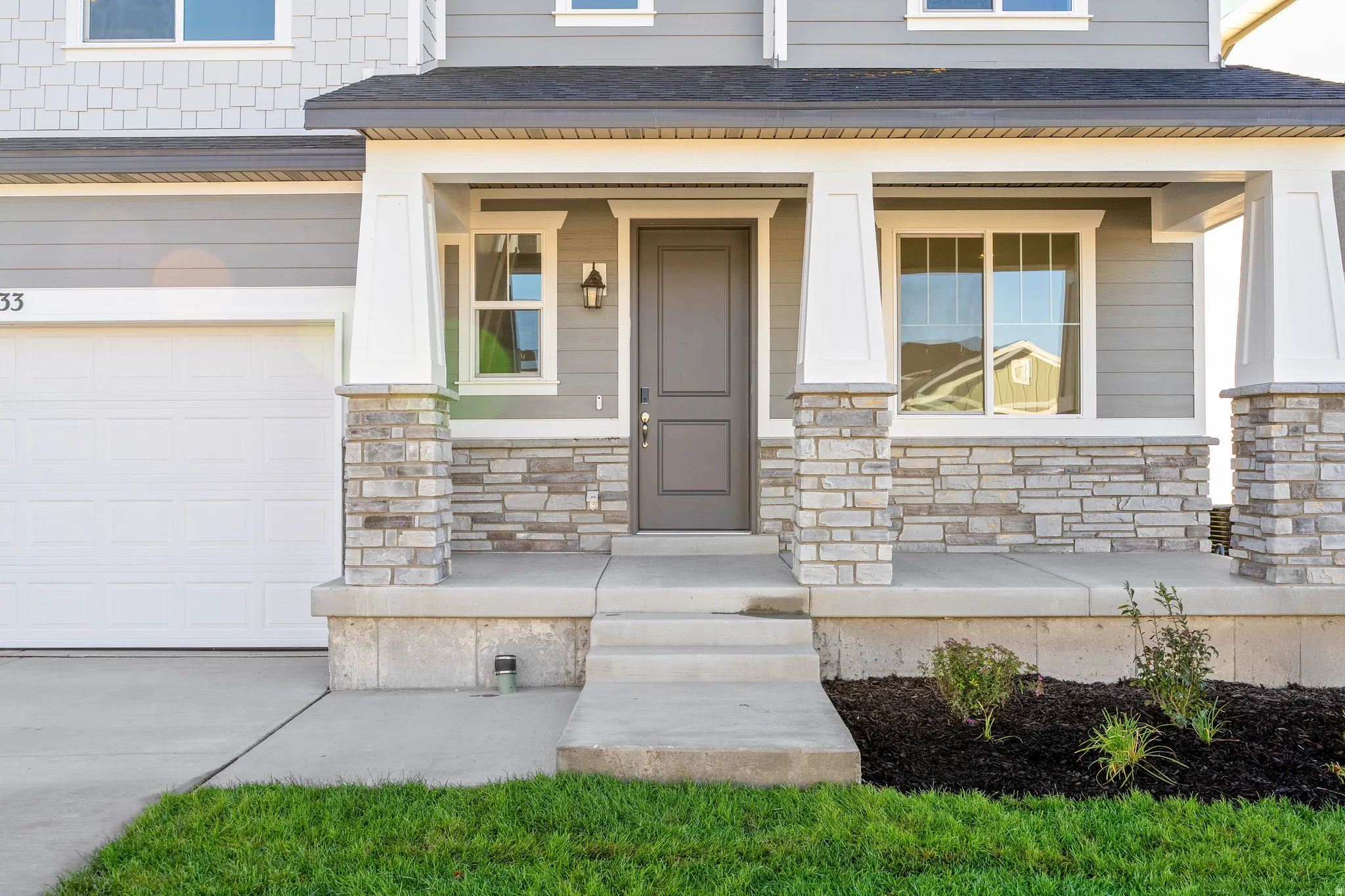 View of exterior entry featuring stone siding, covered porch, a garage, and roof with shingles