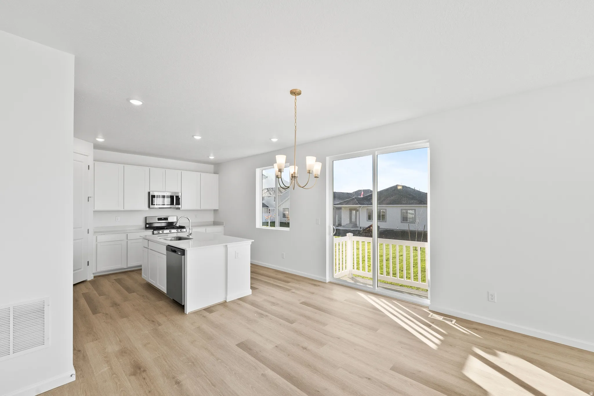 Kitchen with an island with sink, decorative light fixtures, white cabinets, light wood finished floors, and a chandelier