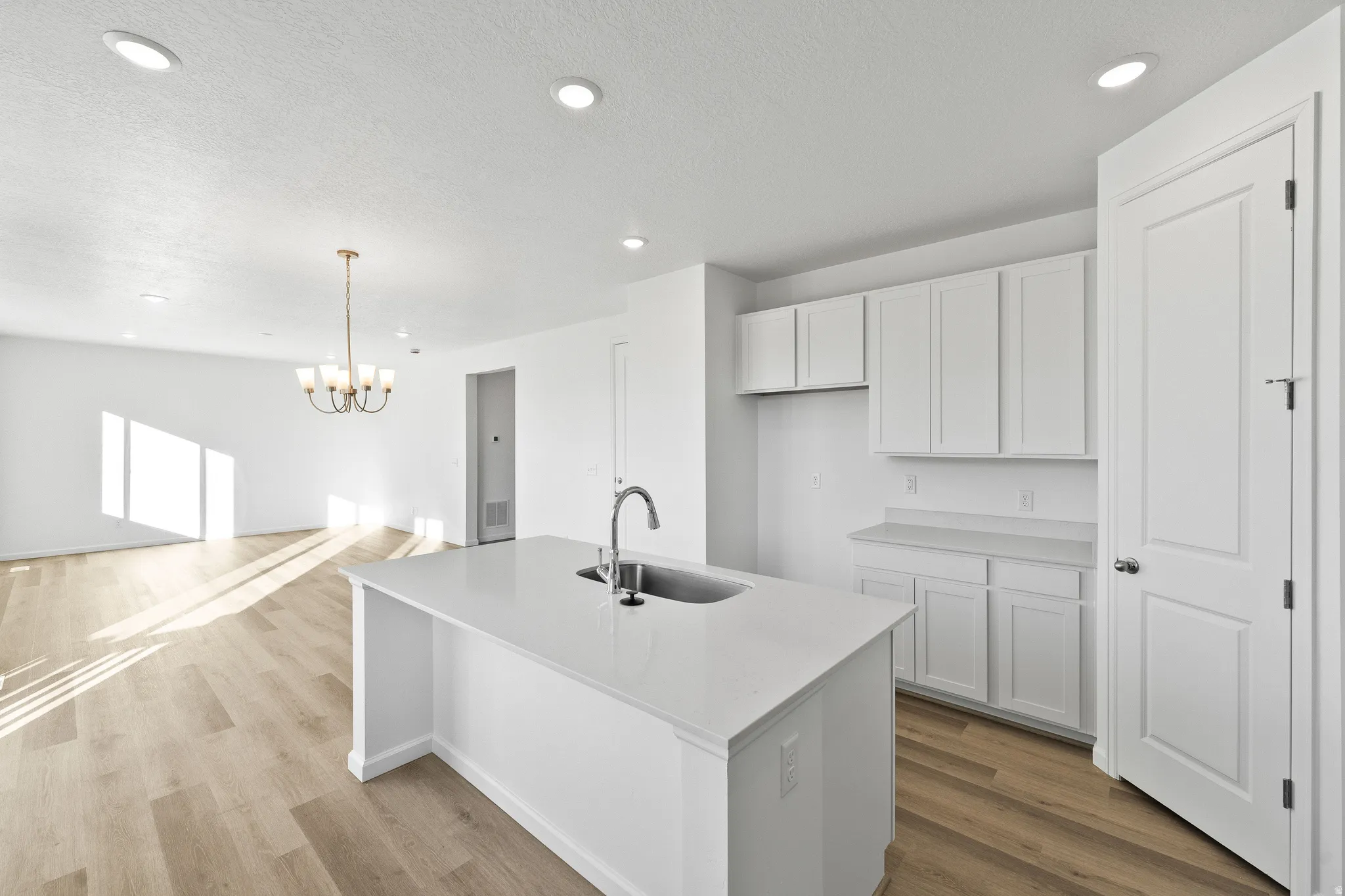 Kitchen with white cabinetry, recessed lighting, decorative light fixtures, an island with sink, and light wood-type flooring