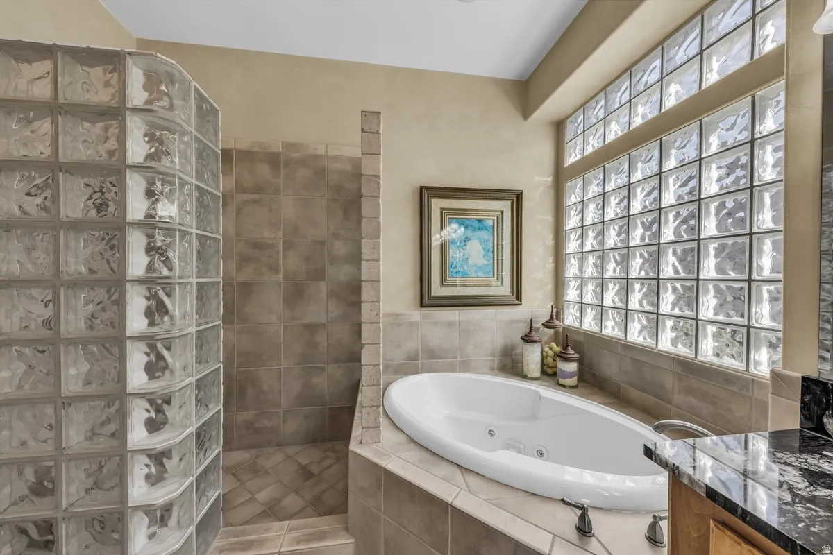 Full bathroom featuring walk in shower, a whirlpool tub, vanity, and tile walls