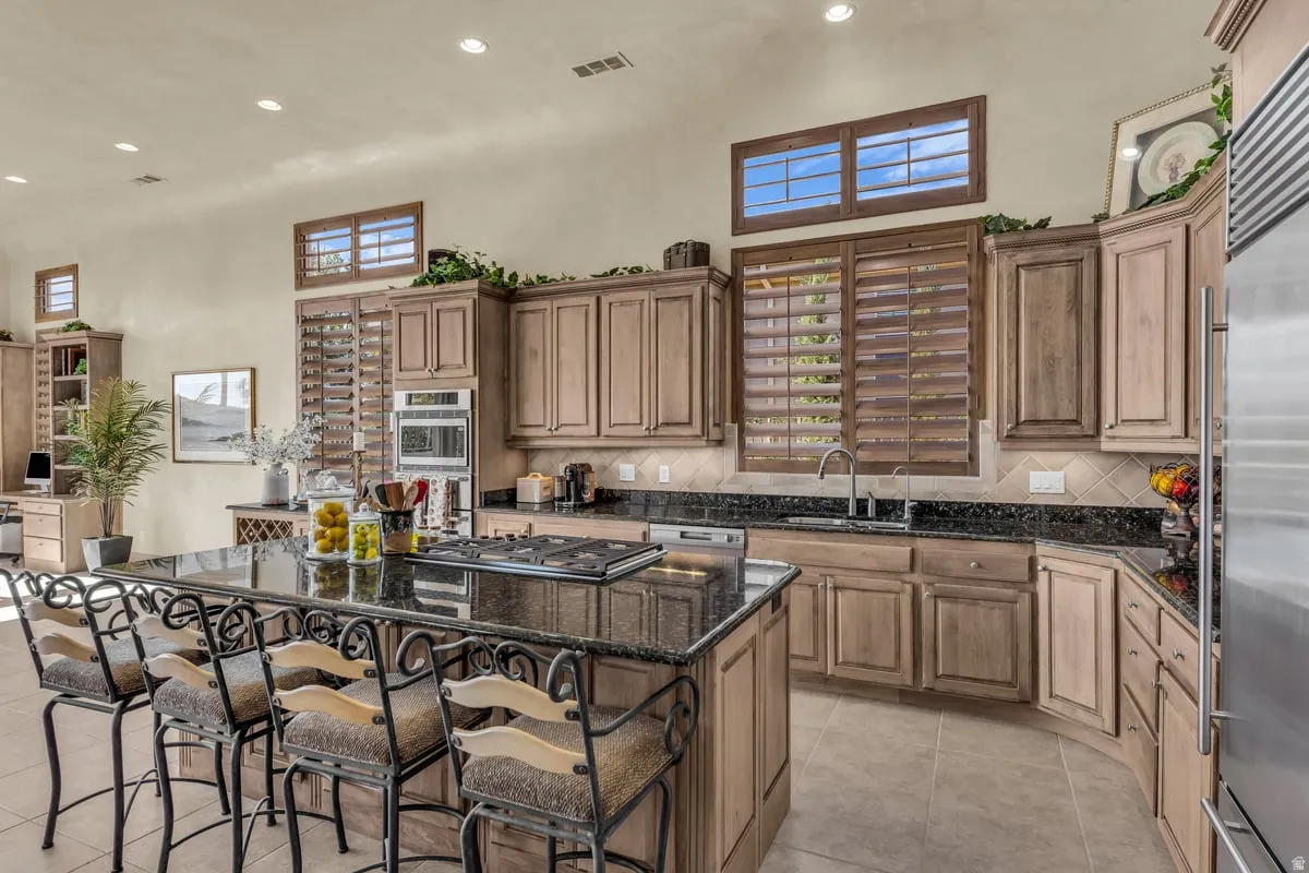 Kitchen featuring recessed lighting, dark stone countertops, decorative backsplash, a kitchen island, and a kitchen breakfast bar