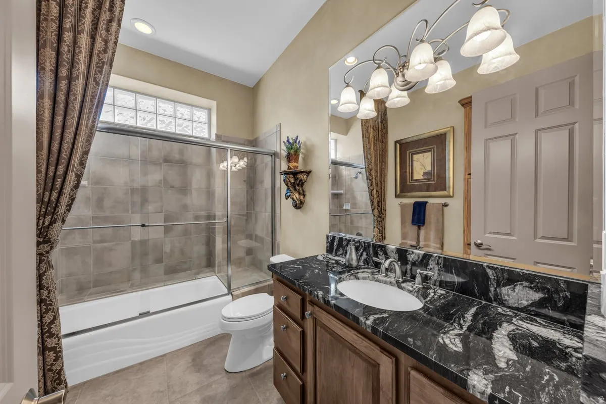 Full bath with bath / shower combo with glass door, vanity, light tile patterned floors, and a chandelier