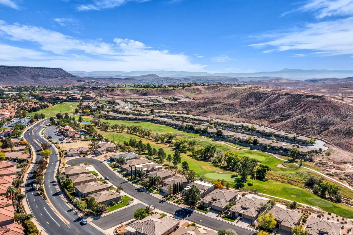 Aerial view of property and surrounding area featuring a mountain backdrop, a golf club, and nearby suburban area