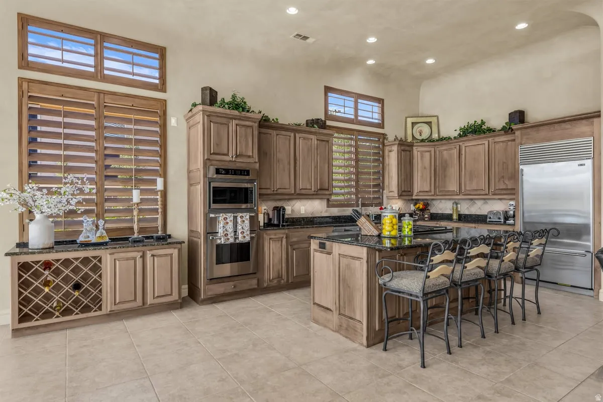 Kitchen with dark stone counters, stainless steel built in refrigerator, a kitchen bar, a center island, and tasteful backsplash