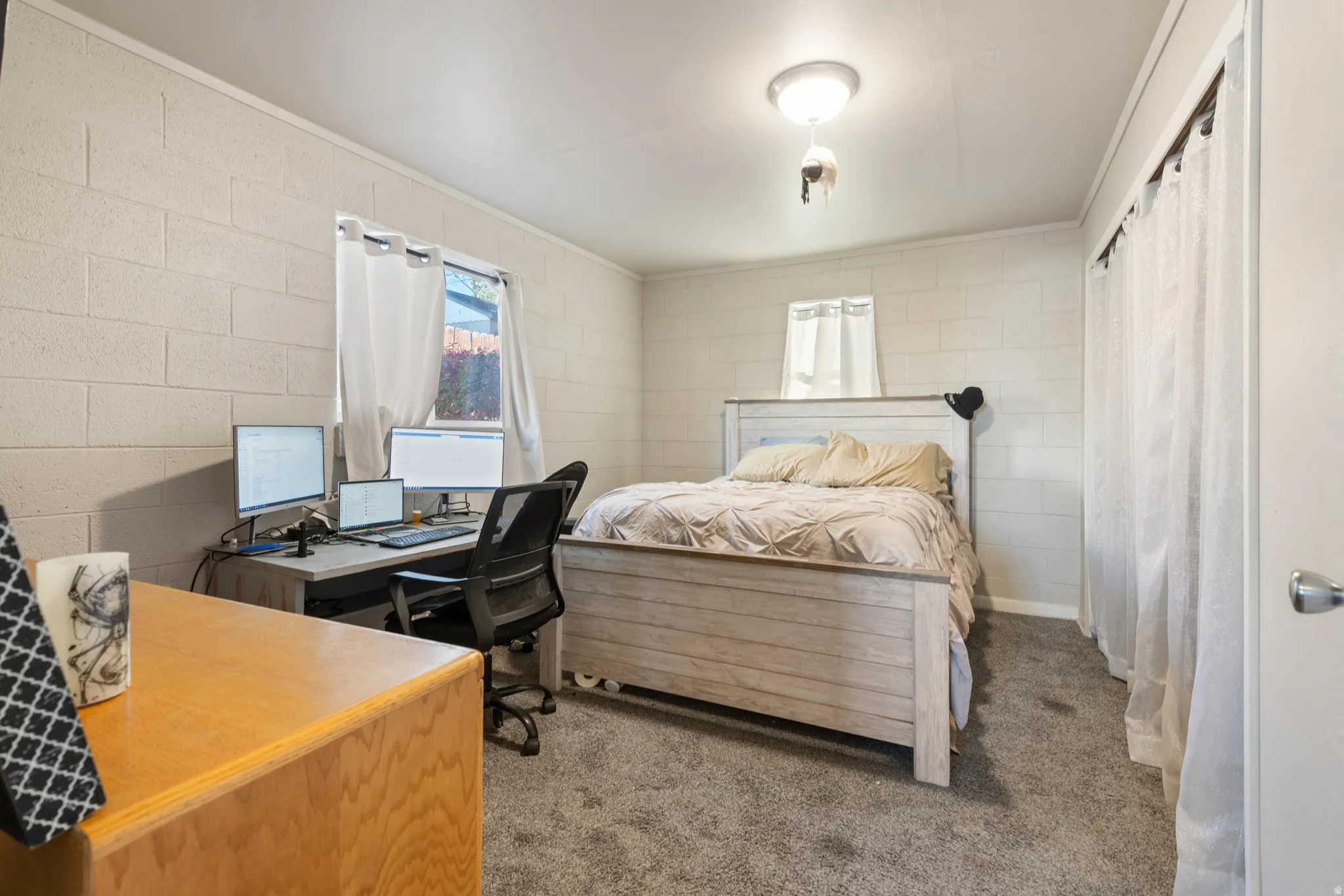 Primary Bedroom with light carpet, concrete block wall, an office area, and ornamental molding