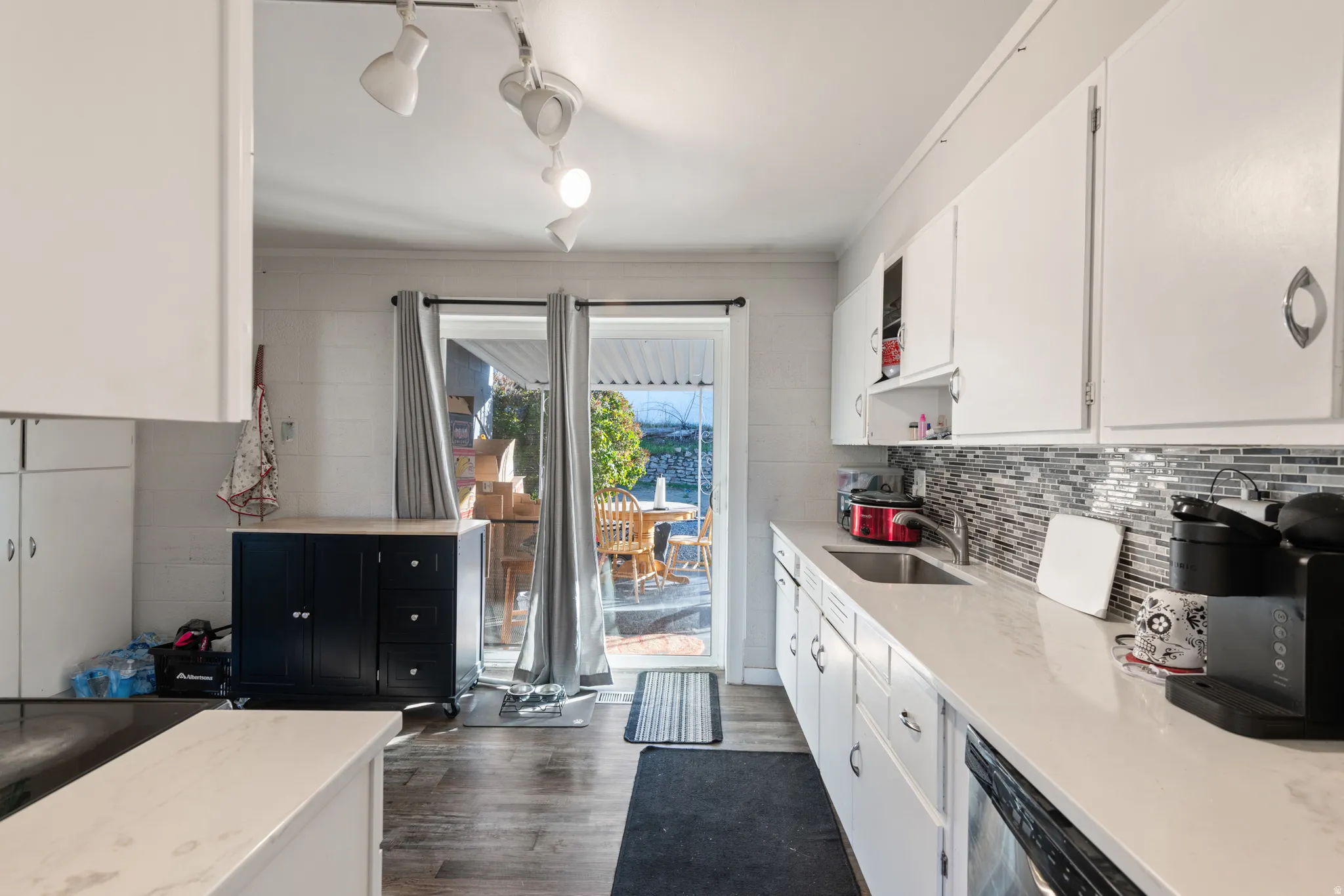 Kitchen with white cabinets, dark wood finished floors, light stone countertops, and stainless steel dishwasher