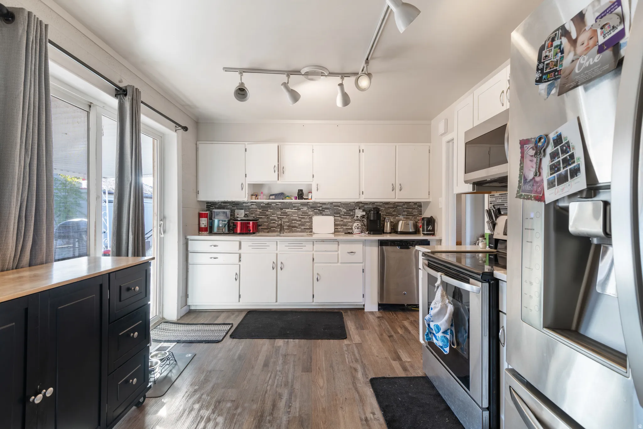Kitchen featuring stainless steel appliances, dark cabinets, decorative backsplash, white cabinets, and dark wood finished floors
