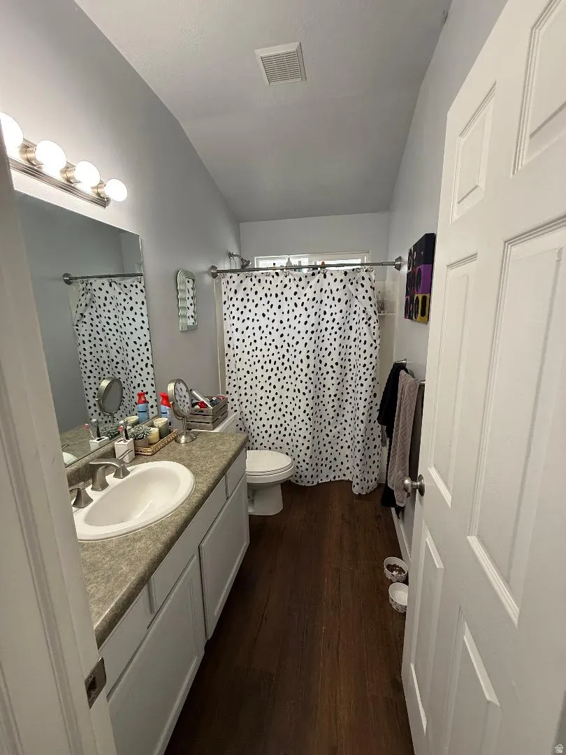 Full bathroom with curtained shower, dark wood-type flooring, and vanity