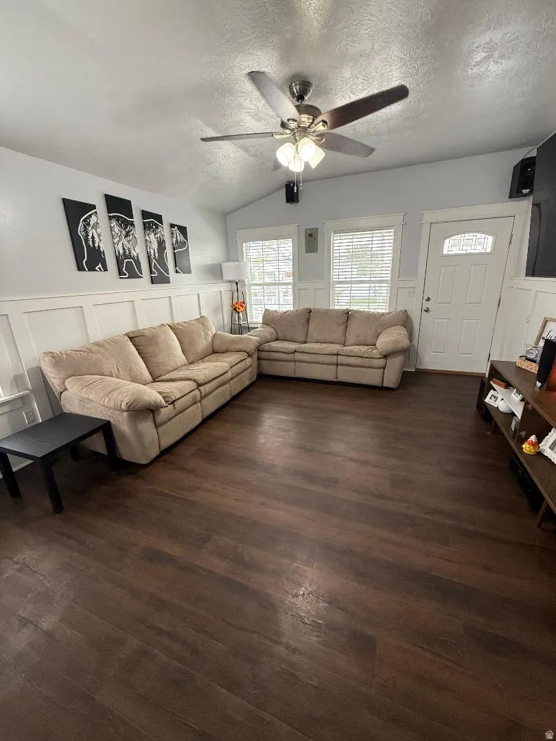 Living area with a decorative wall, a textured ceiling, lofted ceiling, a wainscoted wall, and dark wood-style flooring