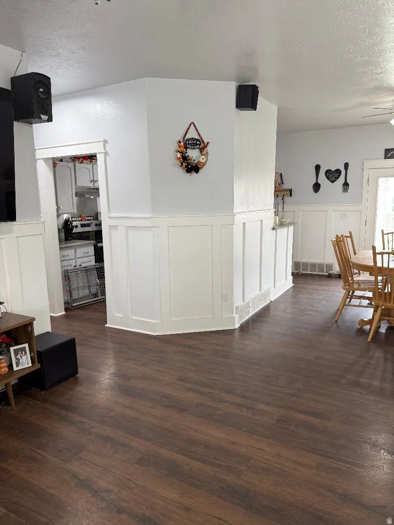 Dining area with a textured ceiling, a decorative wall, dark wood-type flooring, and wainscoting