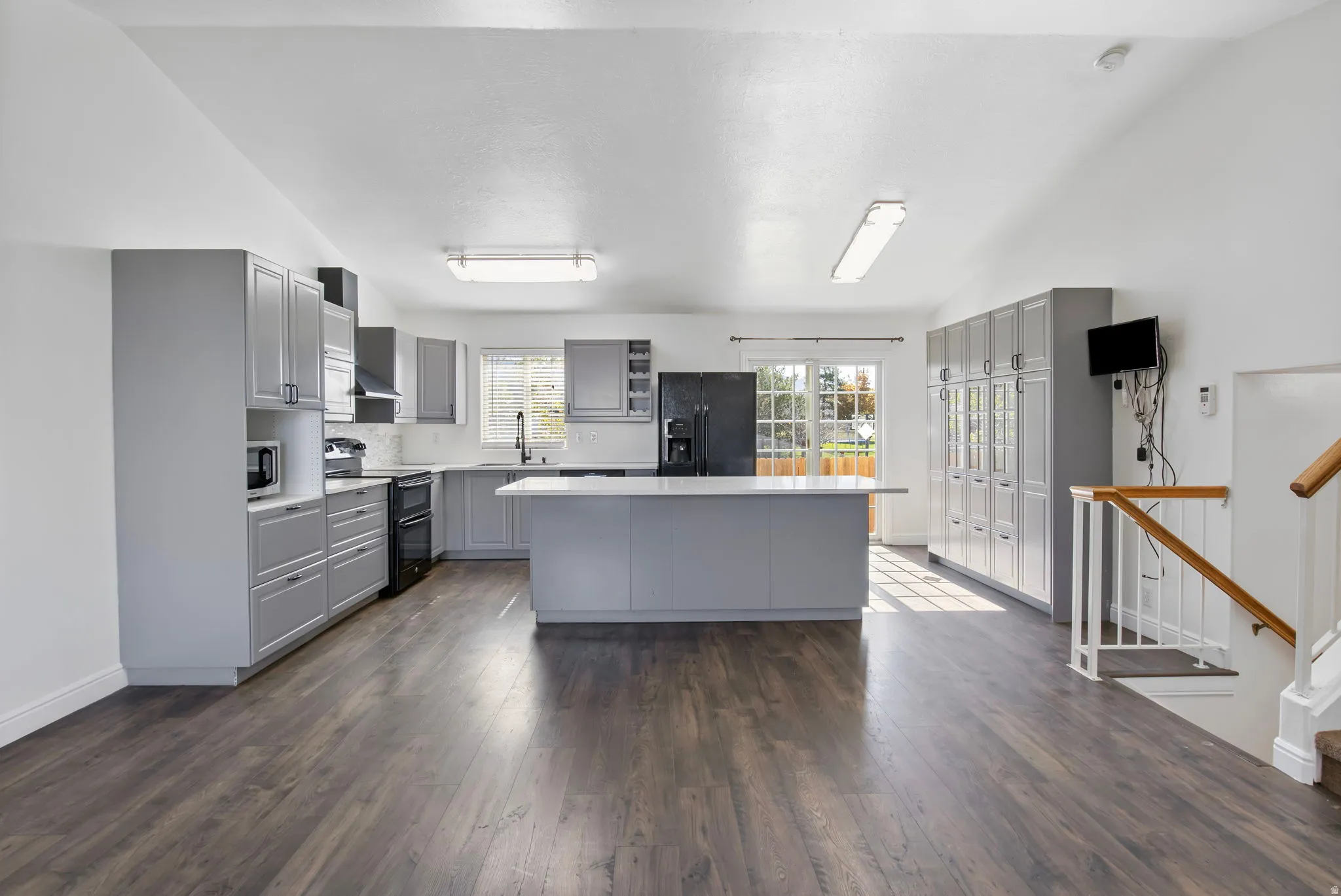 Kitchen featuring gray cabinetry, light countertops, lofted ceiling, black appliances, and dark wood-style floors