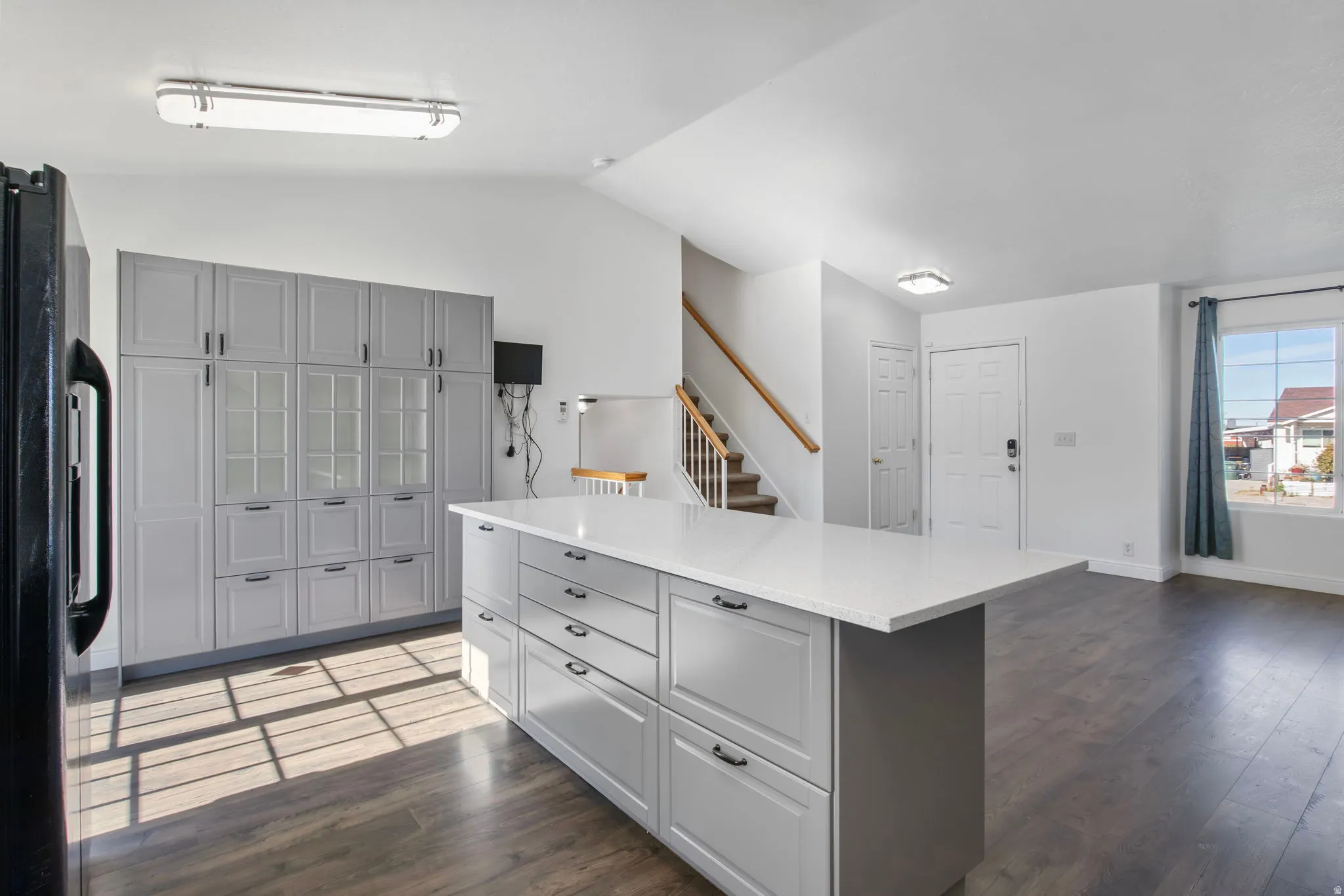 Kitchen with gray cabinets, lofted ceiling, freestanding refrigerator, dark wood-style floors, and a center island